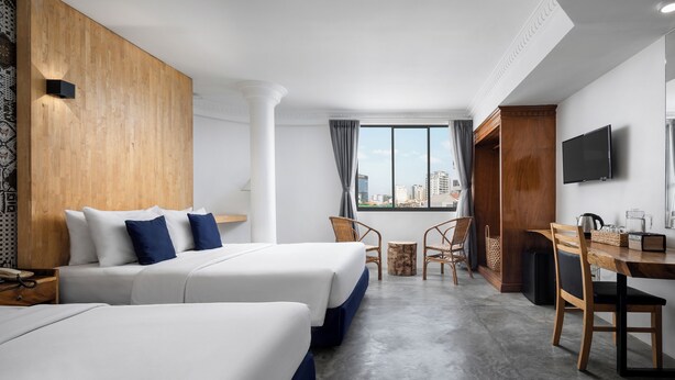 A hotel room with two beds, a dining table, chairs, a TV, and a view of the city through large windows. - Pacific Hotel, Phnom Penh (Phnom Penh)