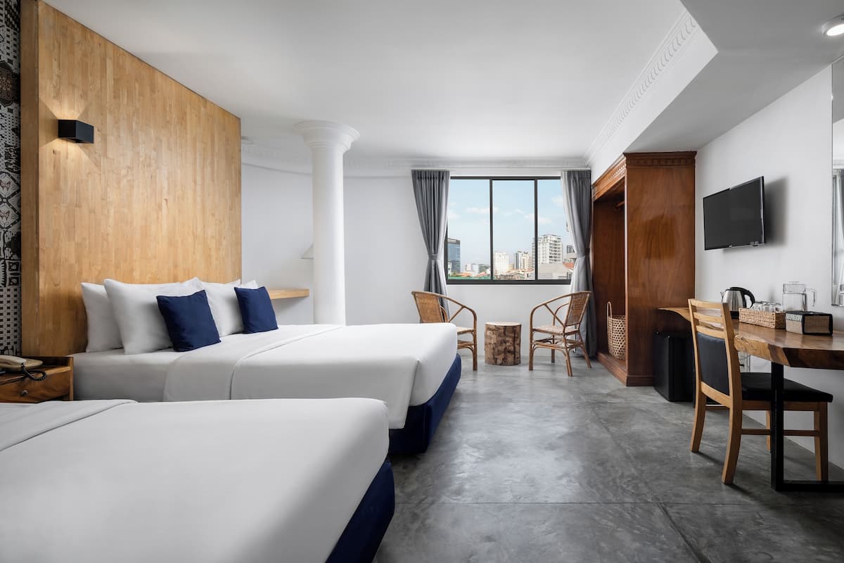 Une chambre d’hôtel avec deux lits, une table à manger, des chaises, un téléviseur et une vue sur la ville grâce à de grandes fenêtres.