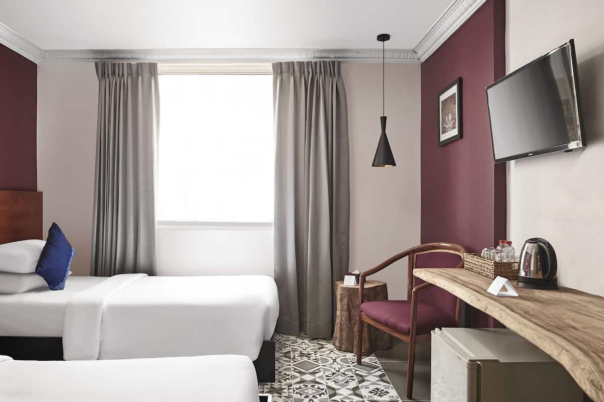 Une chambre d’hôtel avec deux lits, un bureau, une chaise, une télévision et une fenêtre avec des rideaux.