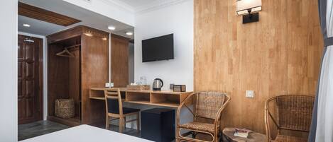 A hotel room with a bed, a desk, two wicker chairs, a television, and a wooden wall.