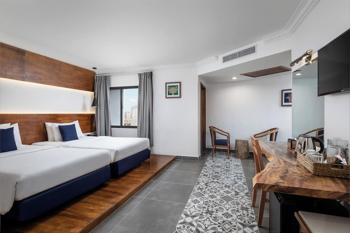 Une chambre d’hôtel avec deux lits, une table à manger, des chaises, un téléviseur et une vue sur la ville.