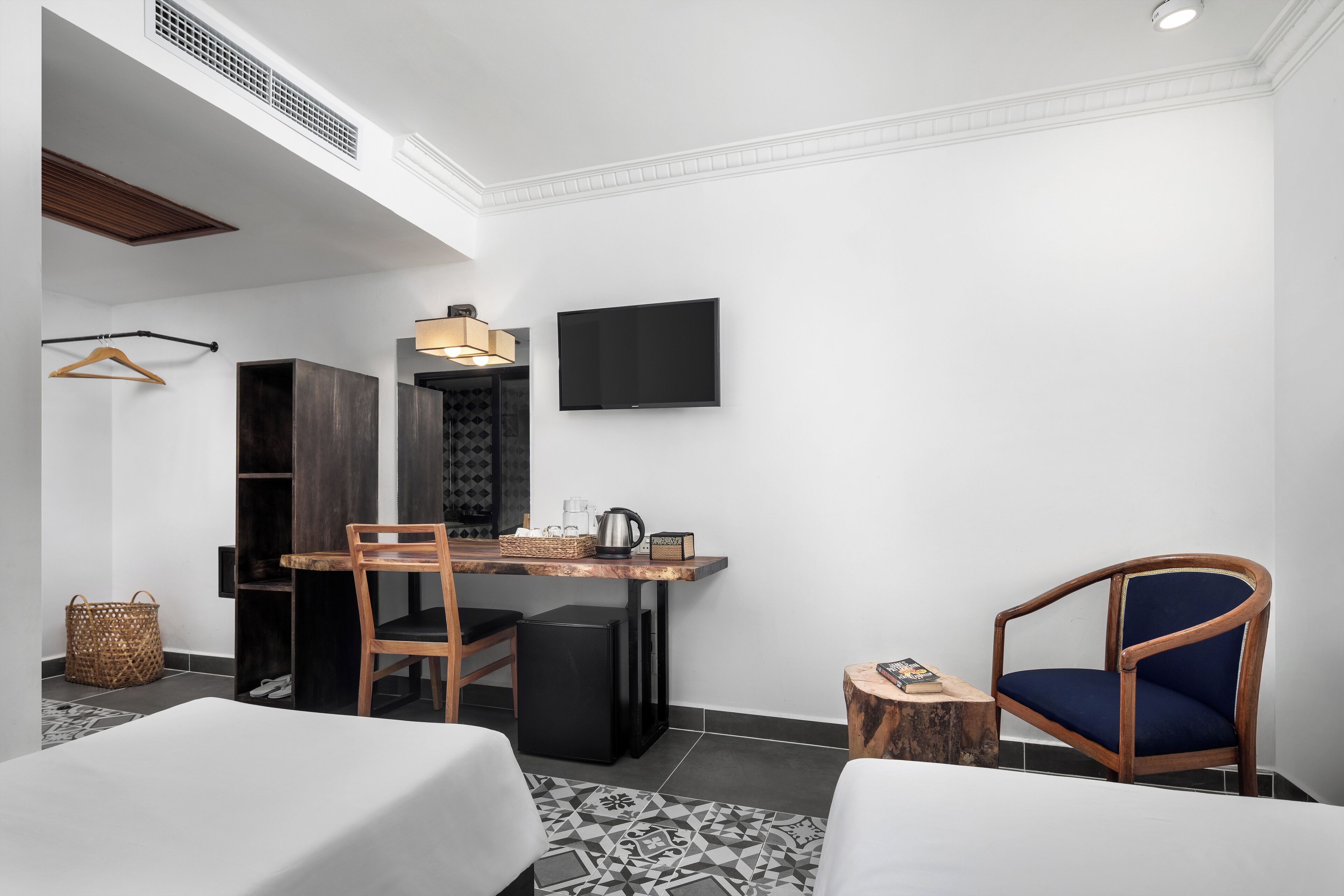 Une chambre d’hôtel moderne, équipée d’un lit, d’un bureau avec une chaise, d’une télévision et d’une petite table sur laquelle se trouve un livre.