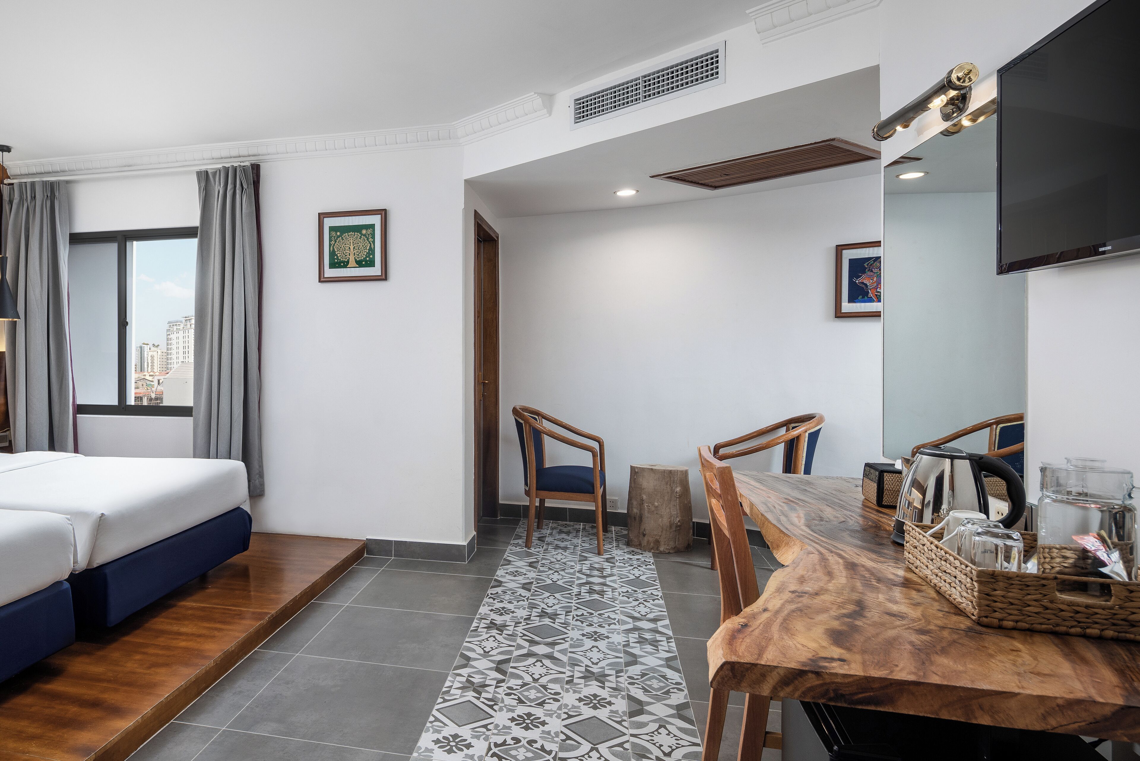 A hotel room with a bed, a dining table, chairs, a TV, and artwork on the walls.