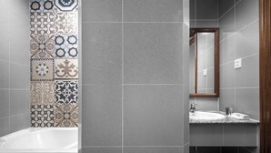 A bathroom with a variety of tile patterns on the walls, a bathtub, a sink, and a mirror. - Pacific Hotel, Phnom Penh (Phnom Penh)