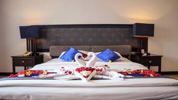 Una cama impecable con sábanas blancas, una disposición de toallas en forma de corazón y almohadas azules.