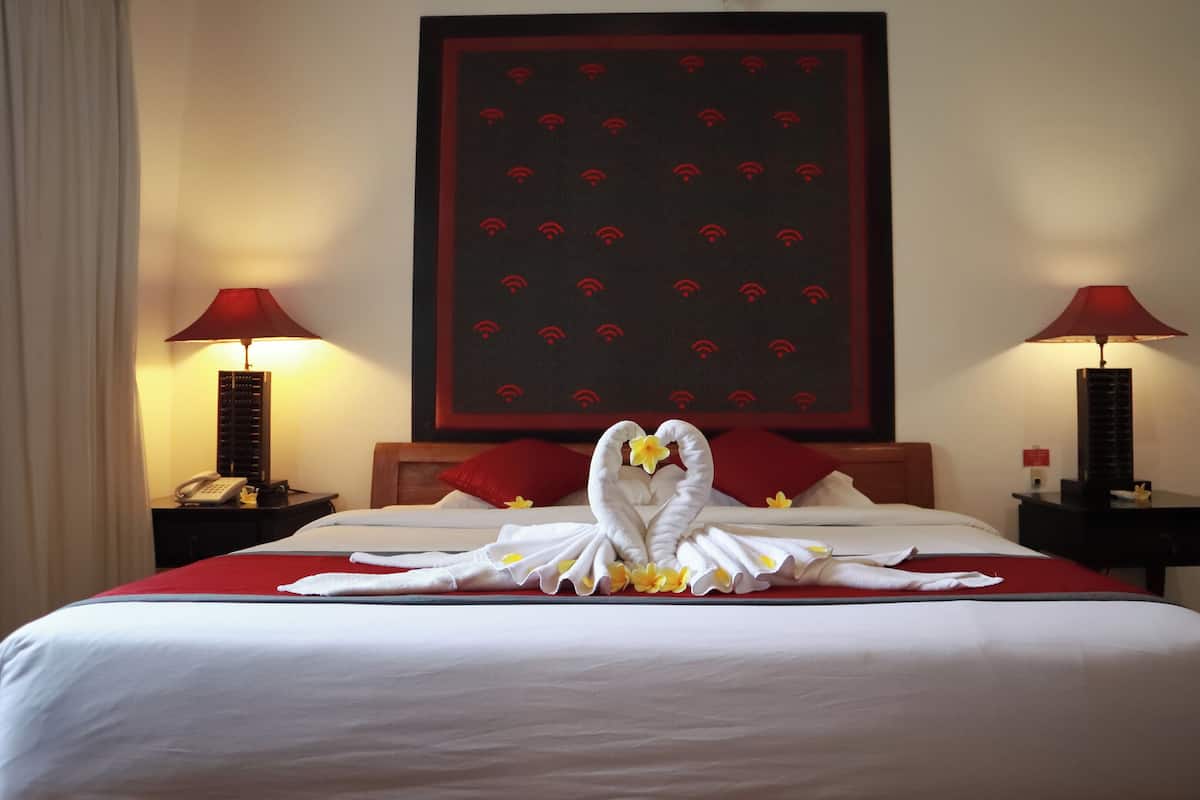 A hotel room with a large bed, two bedside lamps, a telephone, and a wall with a red and black pattern.