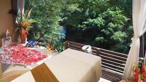 Een balkon met een tafel voor twee personen, omgeven door weelderige begroeiing en uitzicht op een natuurlandschap.
