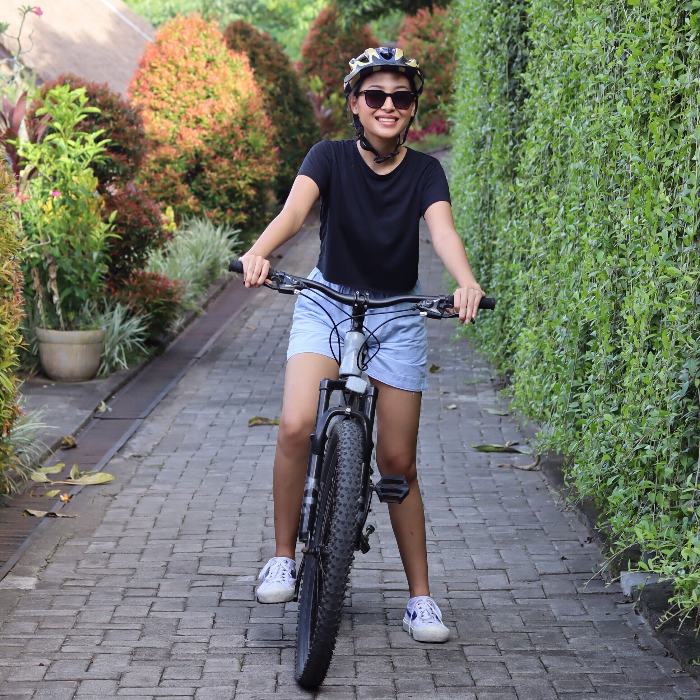A person riding a bicycle on a paved pathway surrounded by greenery.