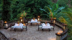 A circular outdoor dining area with tables set for dining, surrounded by lush greenery and stone railings. - Bali Masari Villas & Spa (Sukawati)