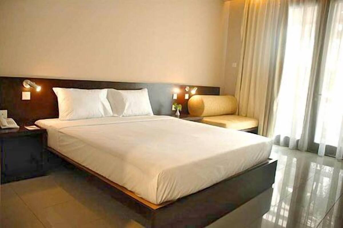A hotel room with a large bed, a nightstand, a bedside table, a sofa, and a window with curtains.