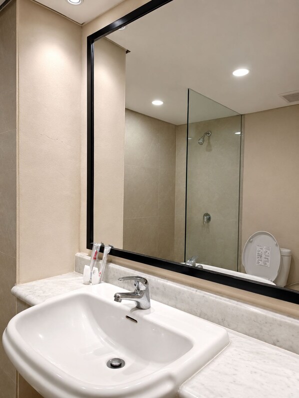 A bathroom with a white sink, a mirror, and a shower. - Grand Tropic Suites Hotel (Jakarta)
