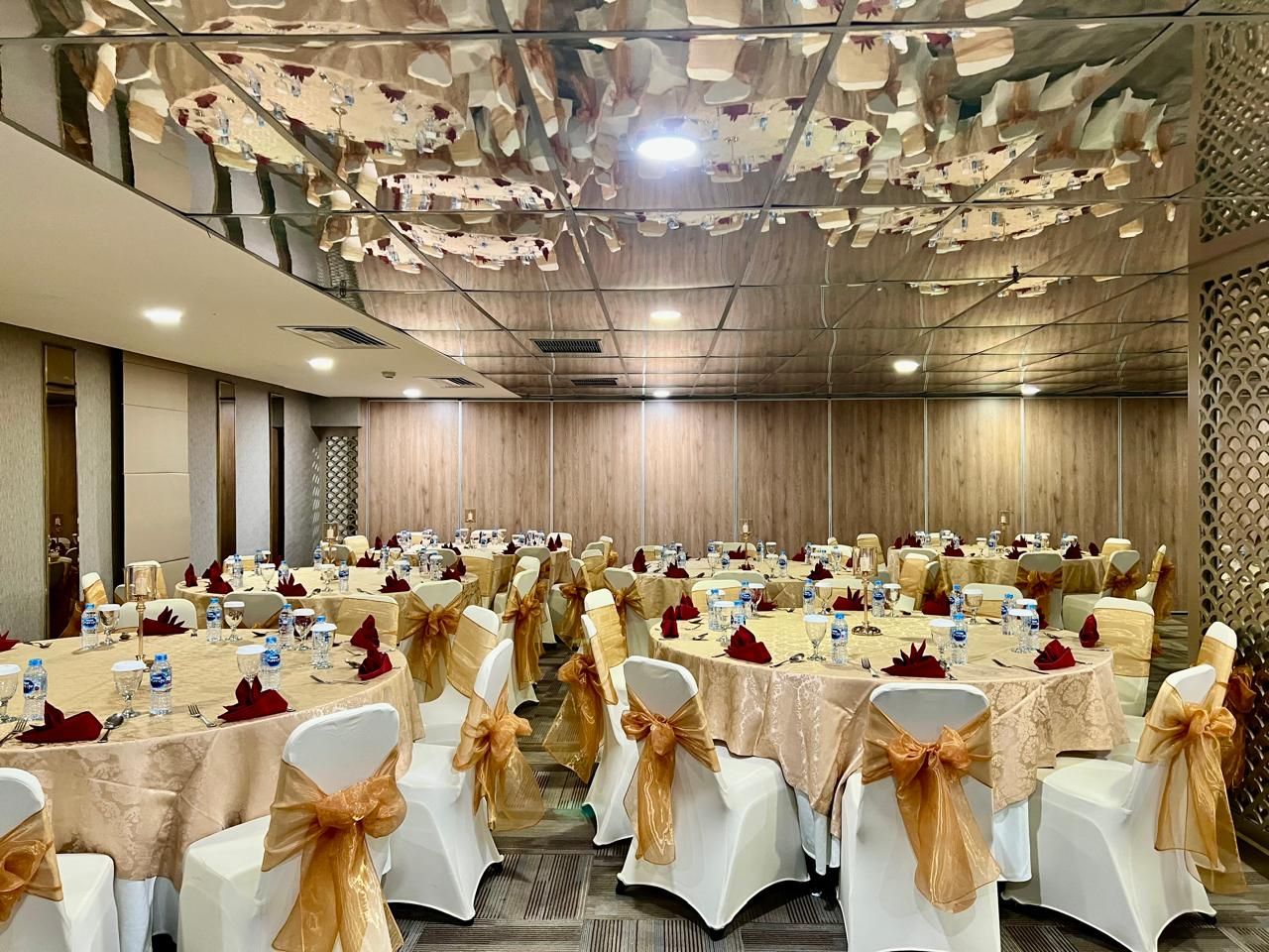 A banquet hall with round tables, white chairs with gold sashes, and a patterned ceiling.