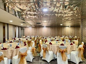 Een feestzaal met ronde tafels, witte stoelen met gouden linten, en een gedessineerd plafond.