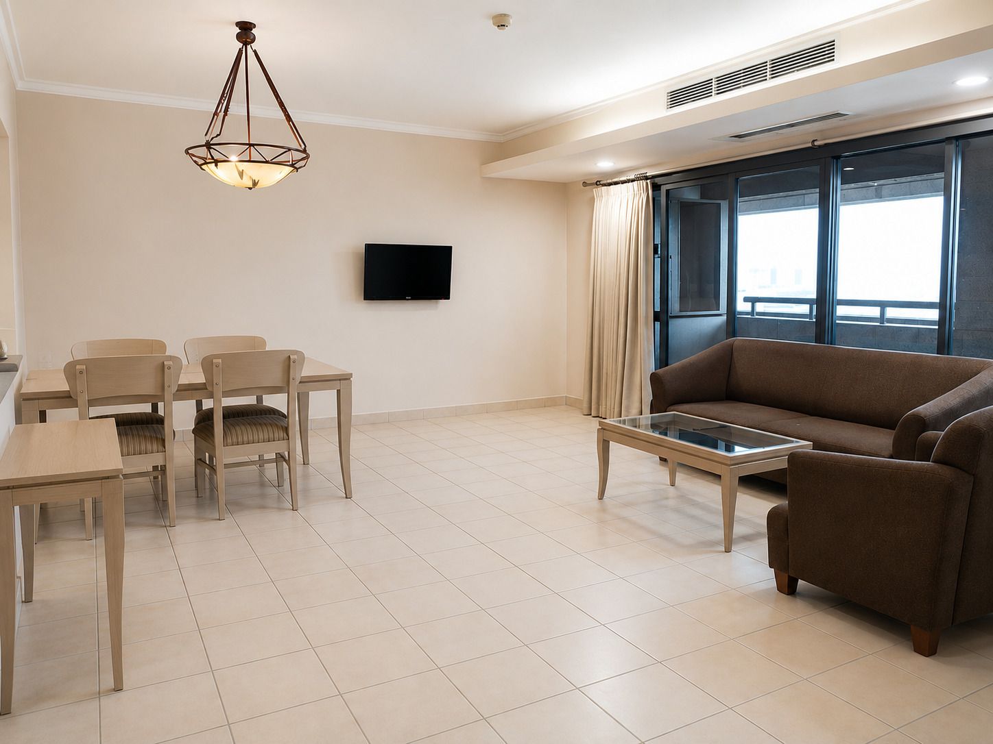 Una sala de estar moderna con un sofá, una mesa de comedor con sillas, una mesa de centro, un televisor de pantalla plana y un amplio ventanal con cortinas.