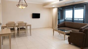 Una sala de estar moderna con un sofá, una mesa de comedor con sillas, una mesa de centro, un televisor de pantalla plana y un amplio ventanal con cortinas.
