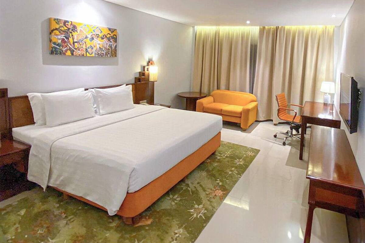 Une chambre d’hôtel avec un grand lit, un bureau, un canapé orange, une télévision et un tableau au mur.