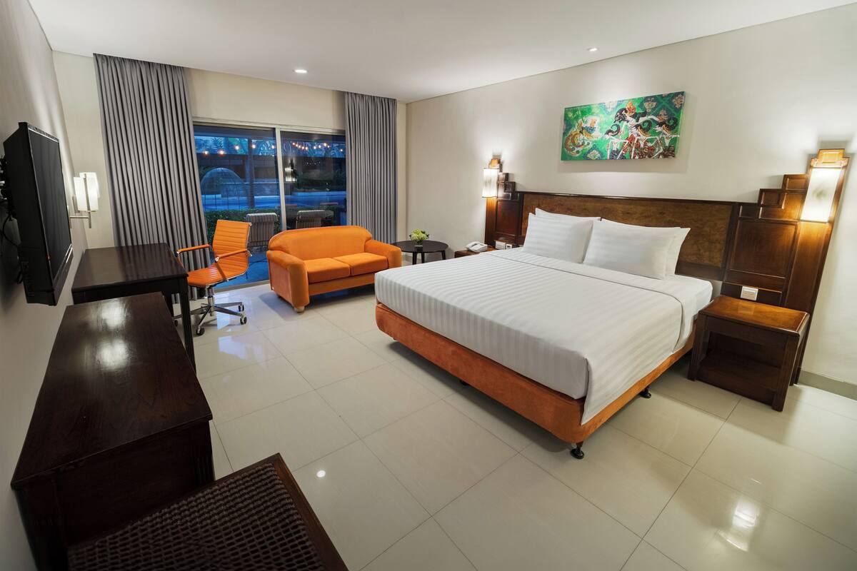 Une chambre d’hôtel avec un lit, un bureau, une chaise, une petite table et un tableau au mur.