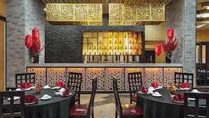 Een restaurant met ronde tafels klaar voor dineren, een decoratieve muur met ingewikkelde patronen en rode lantaarns.