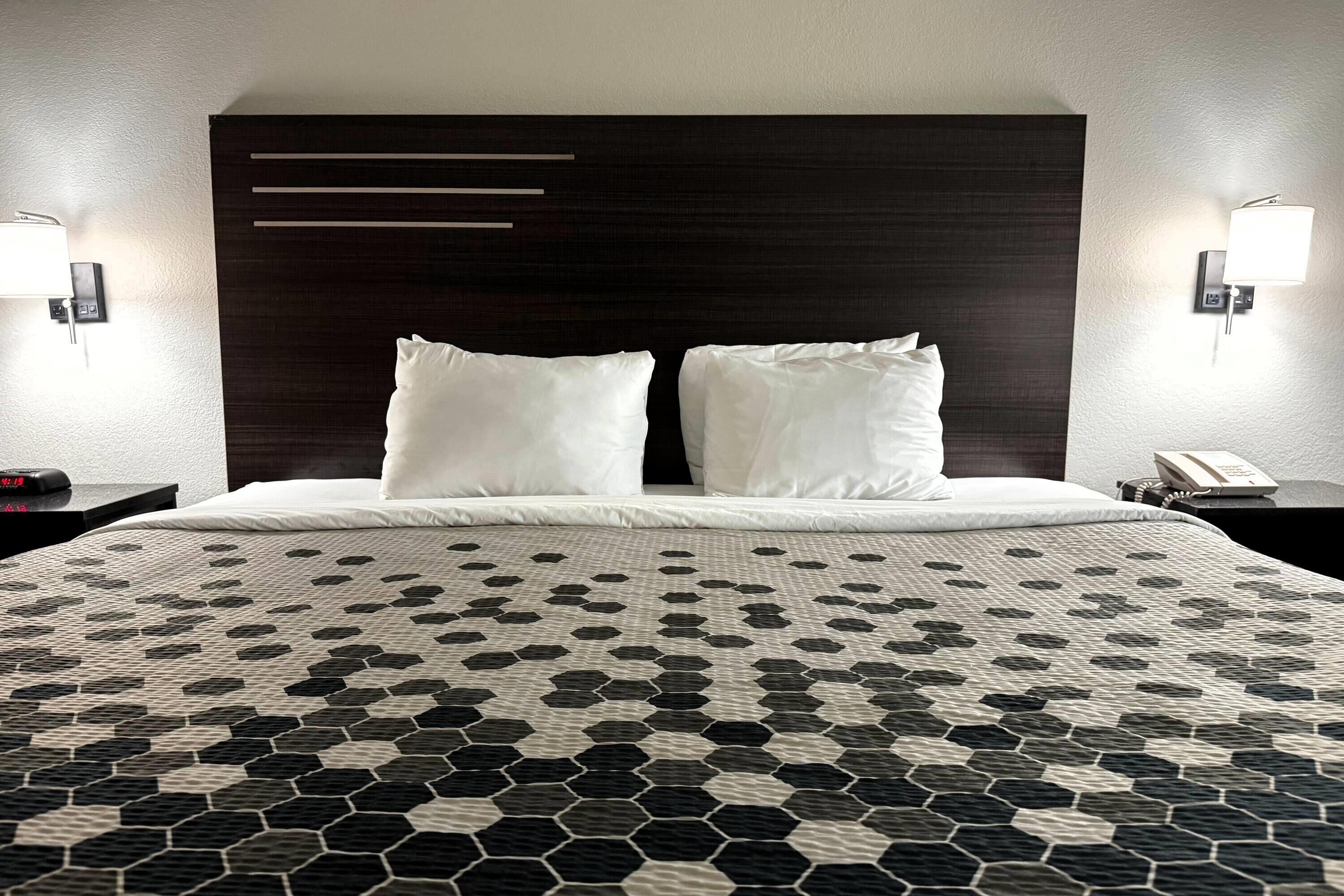 A hotel room with a large bed, two bedside tables, a dark headboard, and wall-mounted lamps.