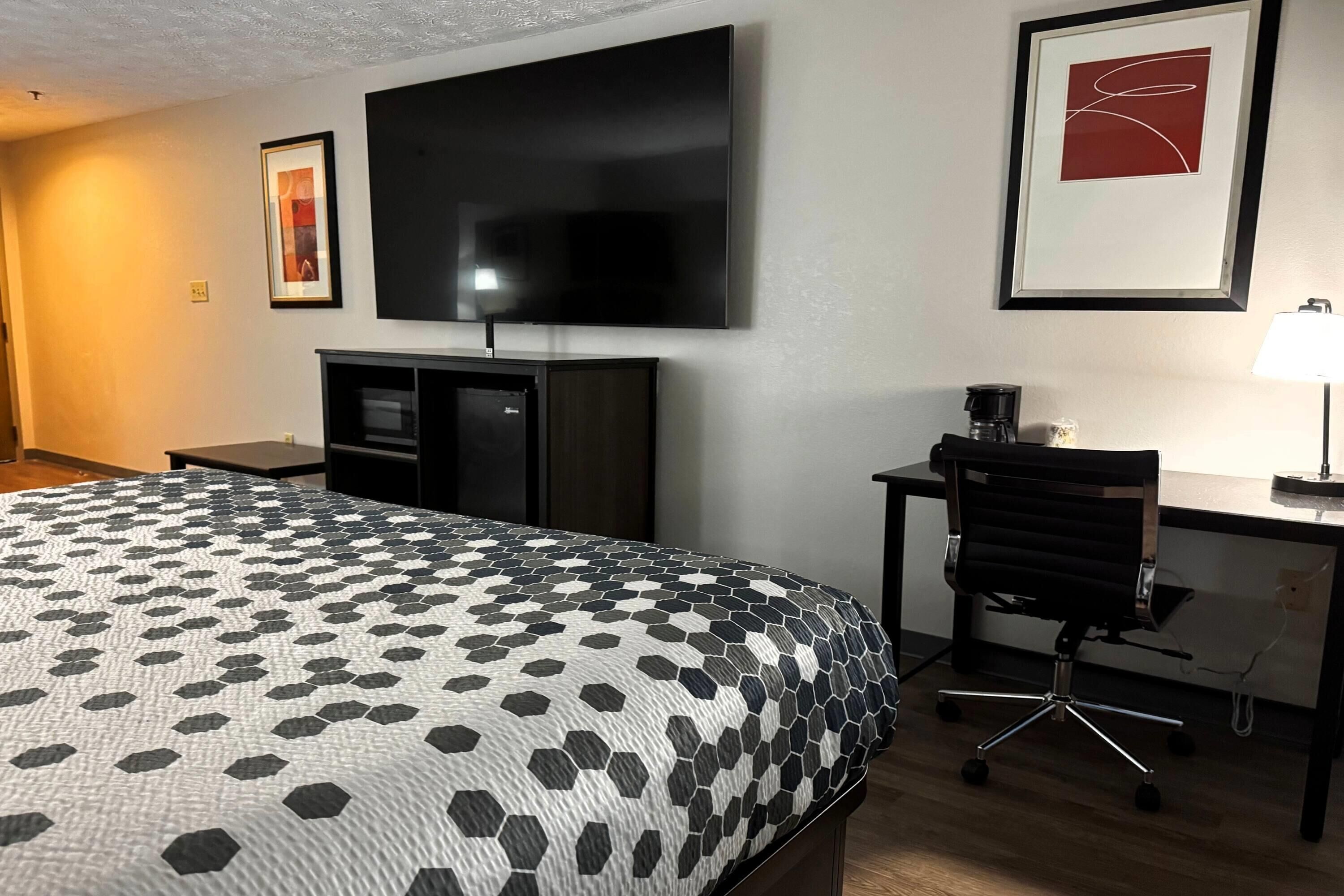 A hotel room with a bed, a desk, a chair, a television, and a framed picture on the wall.