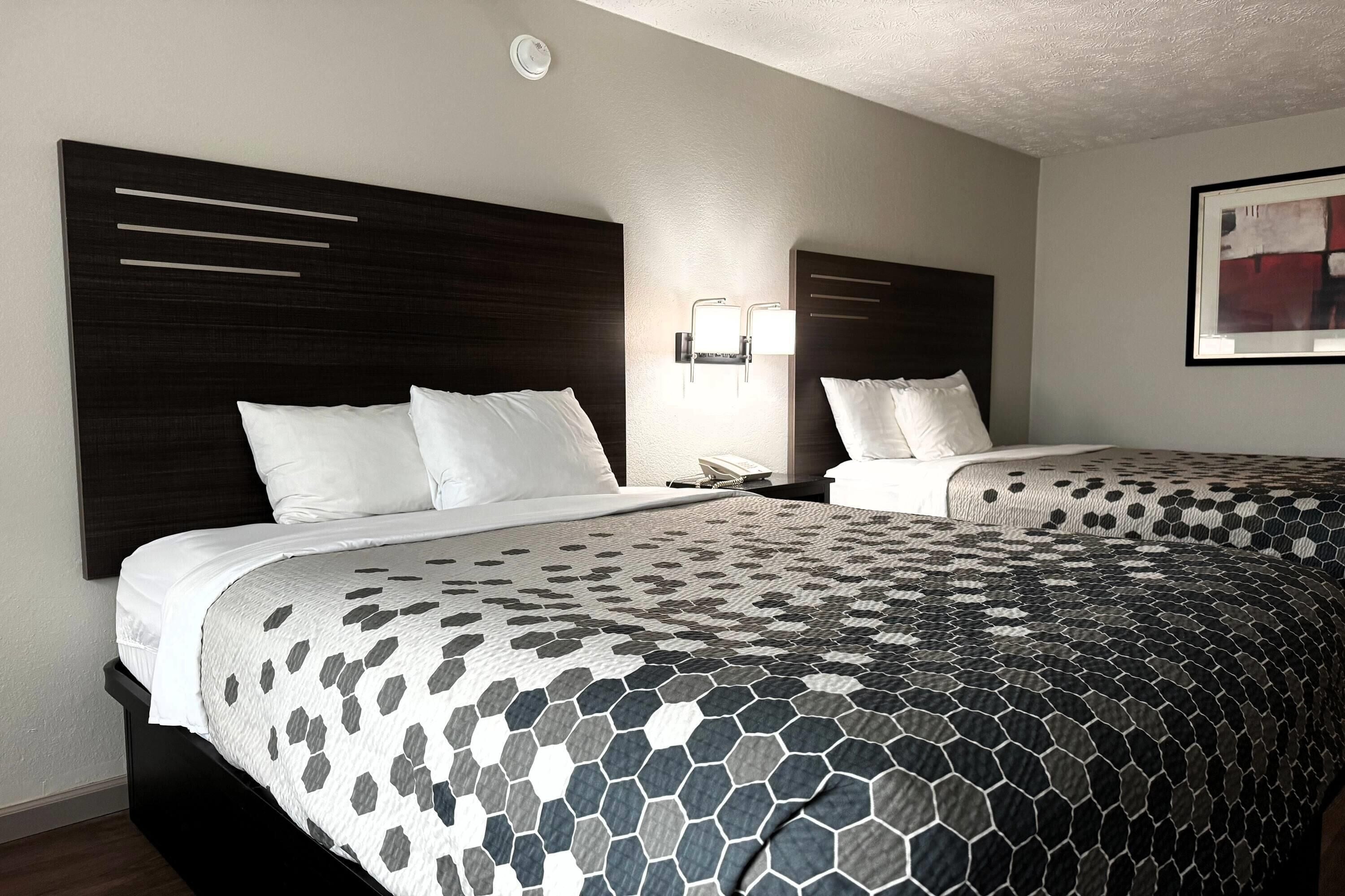 A hotel room with two beds, a modern headboard, a wall-mounted phone, and a framed abstract painting.