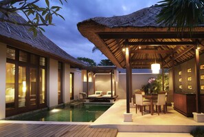 A poolside area with a thatched roof, wooden deck, and a seating area with chairs and a table. - Villa Mahapala (Denpasar)