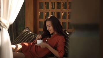 A person sitting on a bed with a cup, in a room with a wooden lattice partition and a curtain.