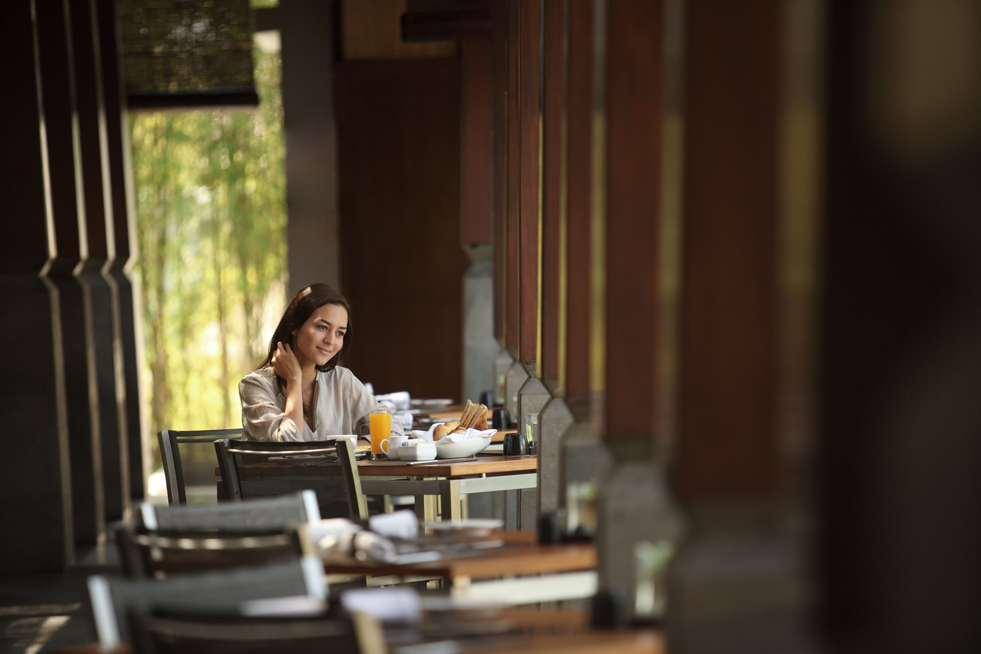 A person sitting at a table with breakfast items, including a bowl of cereal, a cup of coffee, and a glass of orange juice.