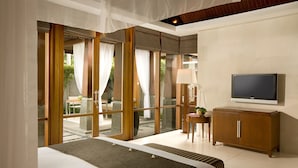 Ein modernes Hotelzimmer mit einem großen Bett, einem Fernseher, einem Holzschrank und einer Glastür zu einem Außenbereich.