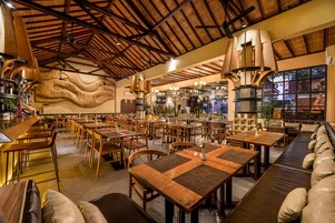 Un restaurante espacioso con techos altos, mesas y sillas de madera, y un gran mural en la pared.