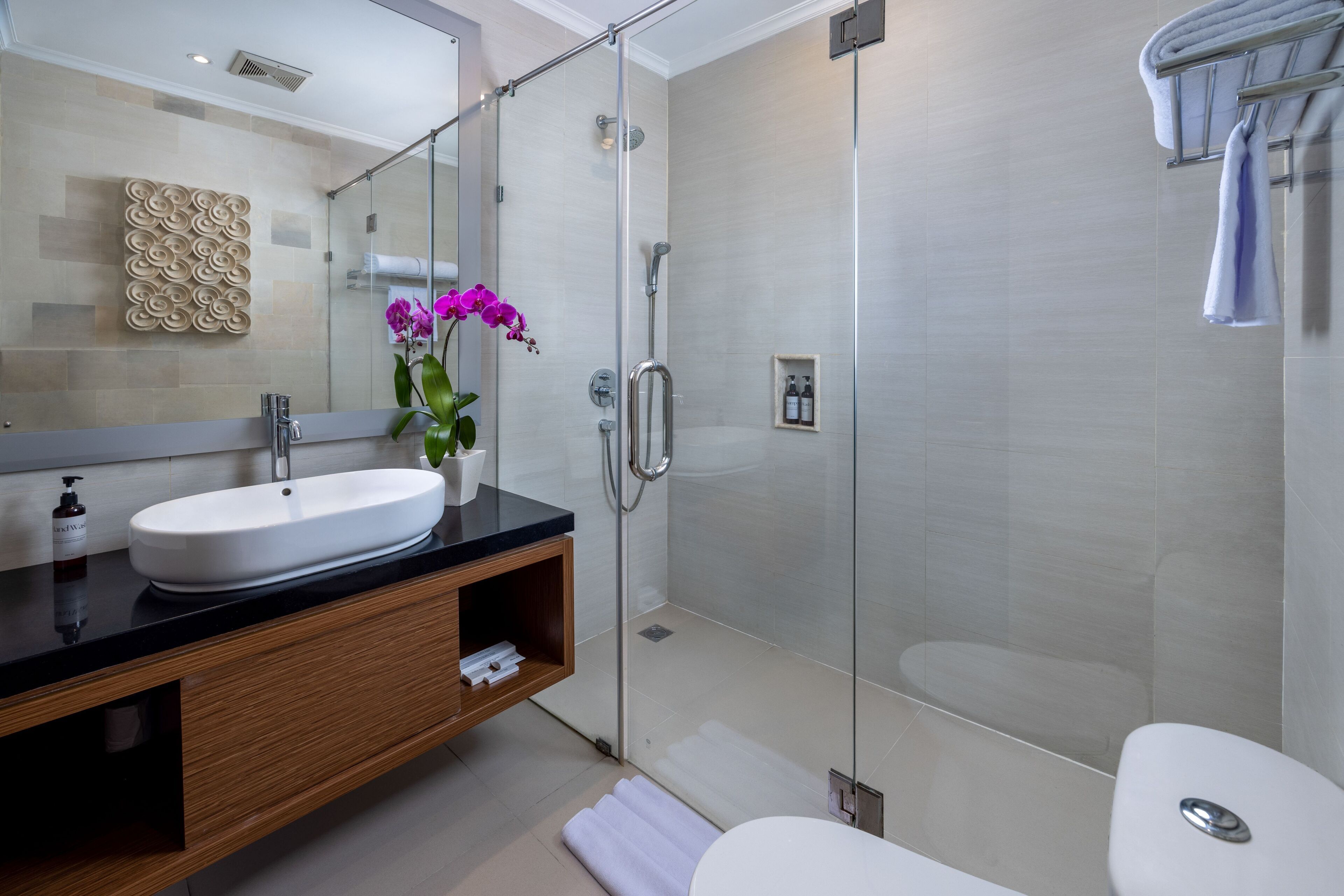 A modern bathroom with a glass-enclosed shower, a white sink, and a wooden vanity.