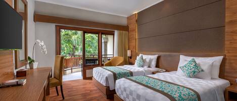 A hotel room with two beds, a desk, a chair, and a balcony with a view of greenery.