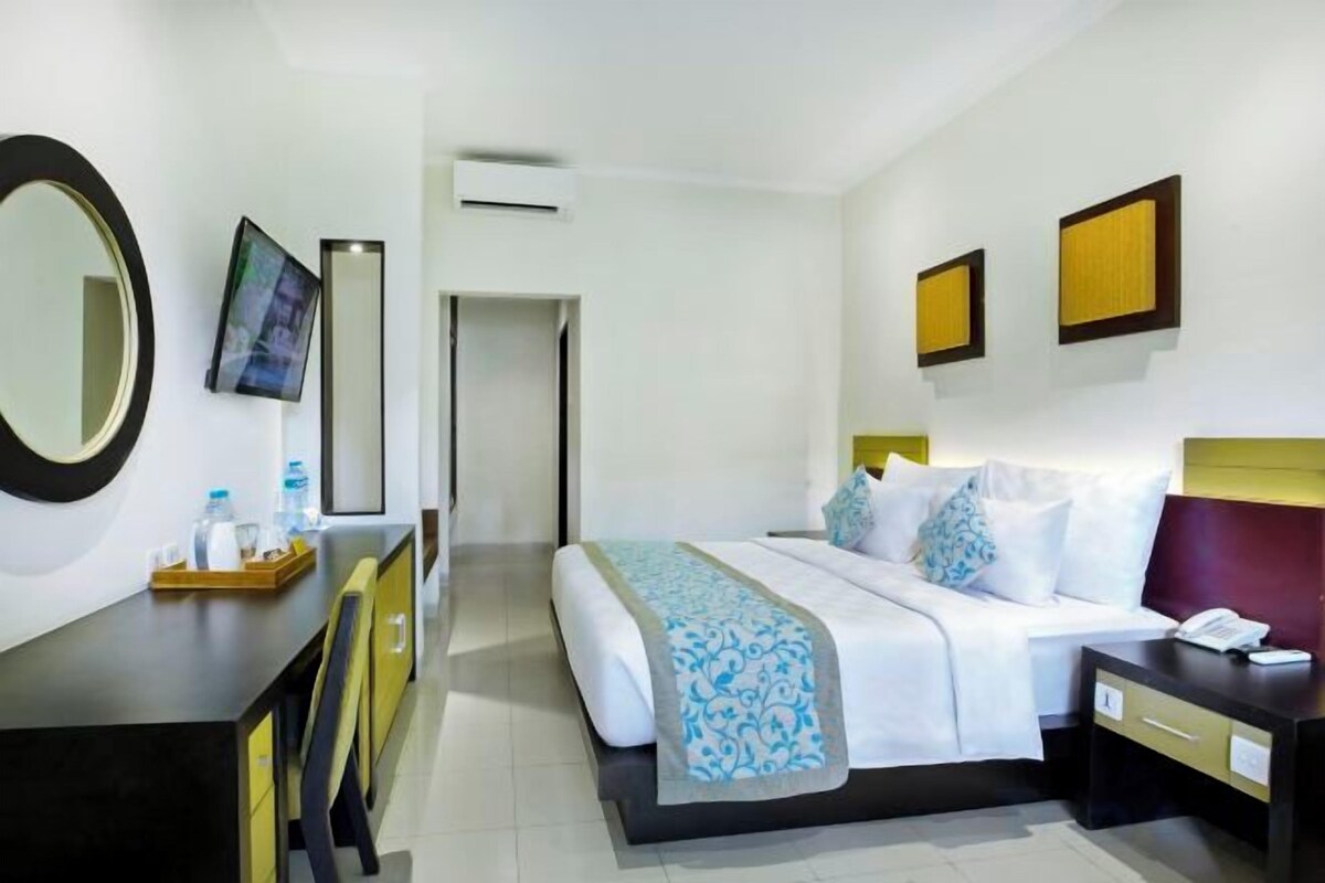 A hotel room with a bed, bedside table, desk, chair, and a mirror.