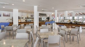 Uma ampla área de jantar com várias mesas e cadeiras, um bar central e uma cozinha ao fundo.