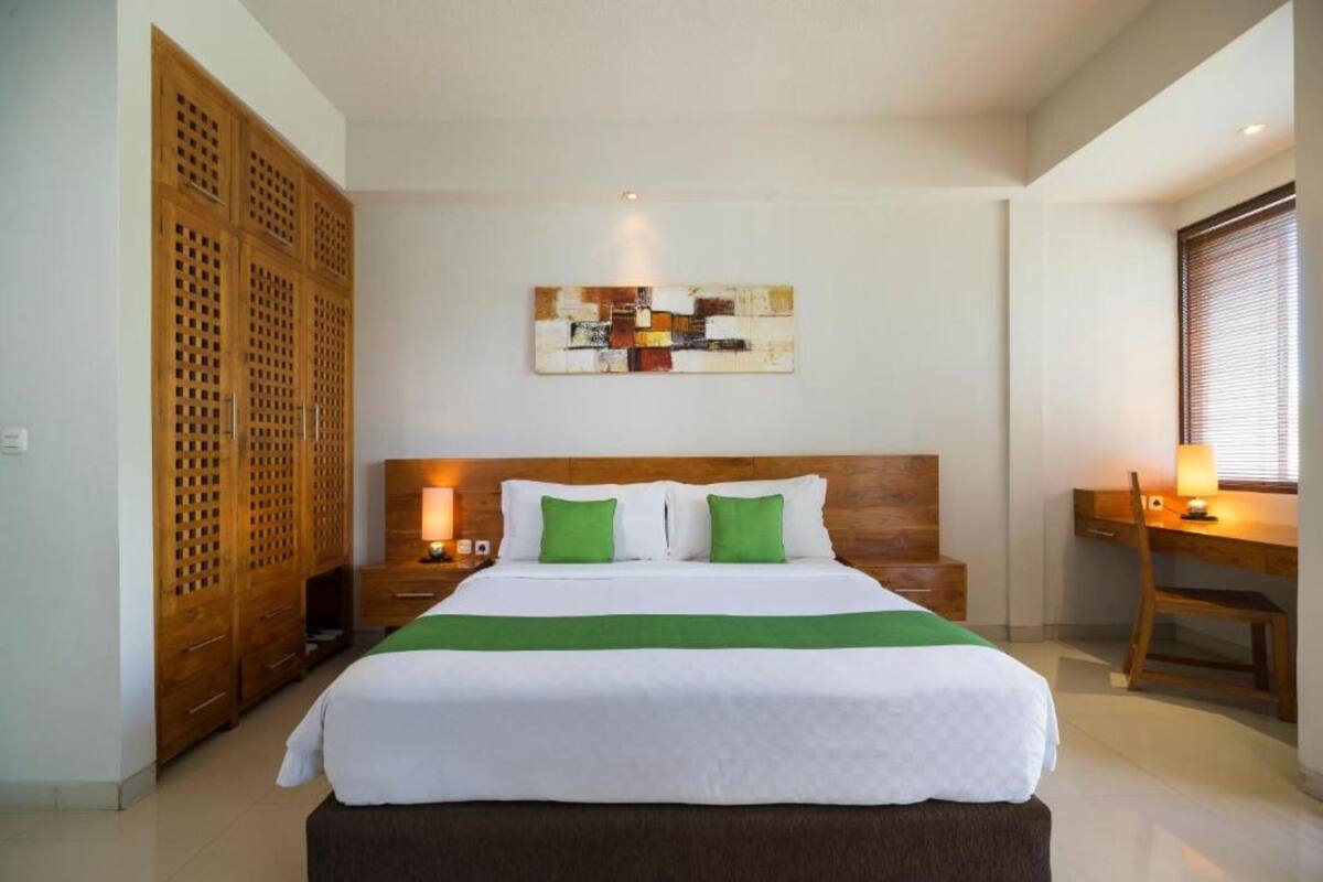 Ein Hotelzimmer mit einem großen Bett, einem Holz-Kopfteil, einem Schreibtisch mit Stuhl und einem an der Wand hängenden Kunstwerk.