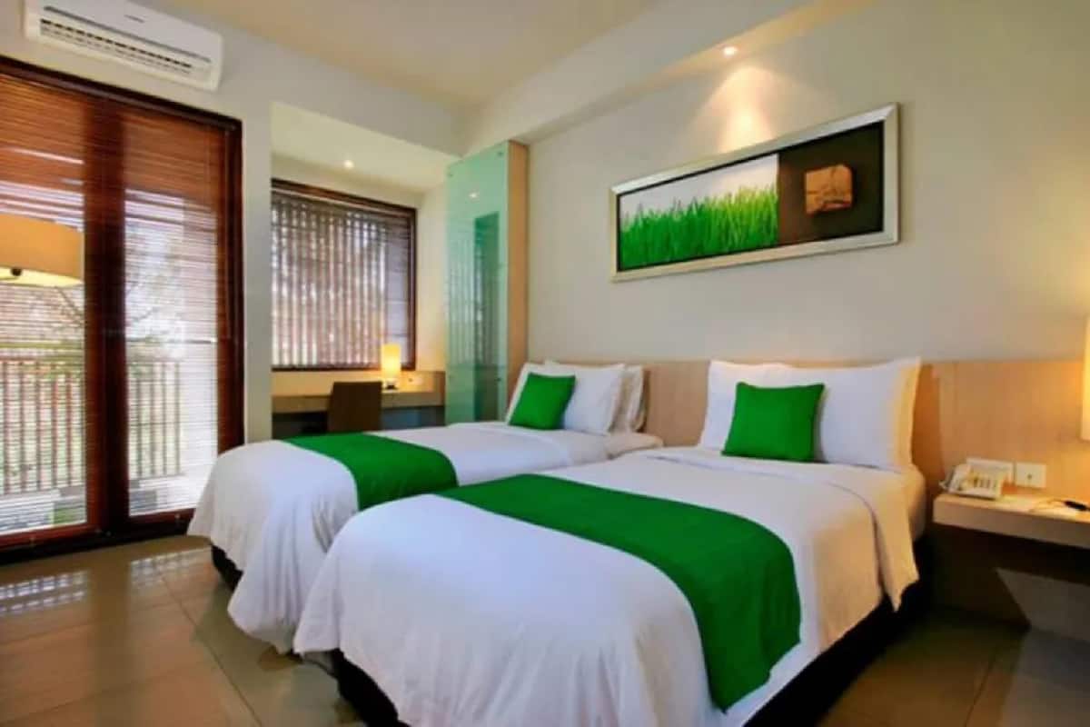 Ein Hotelzimmer mit zwei Betten, einem Schreibtisch, einem Stuhl, einem Fenster mit Jalousien und einem Bild an der Wand.