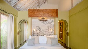 A spacious bedroom with a large bed, a wooden ceiling beam, and a tropical mural on the wall.