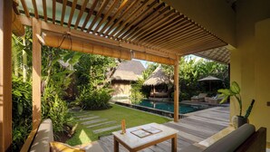 A wooden deck with a pool, a thatched-roof structure, and lush greenery.