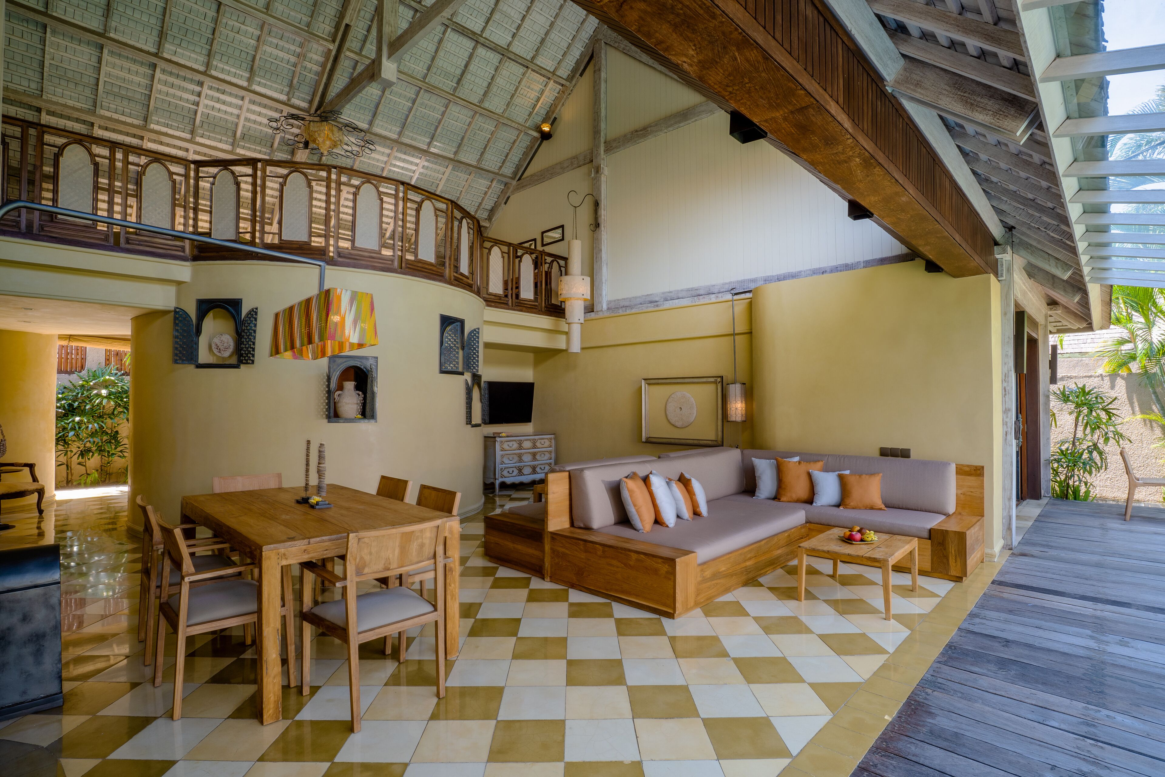 A spacious indoor area with a wooden dining table and chairs, a sofa with cushions, and a checkered floor.