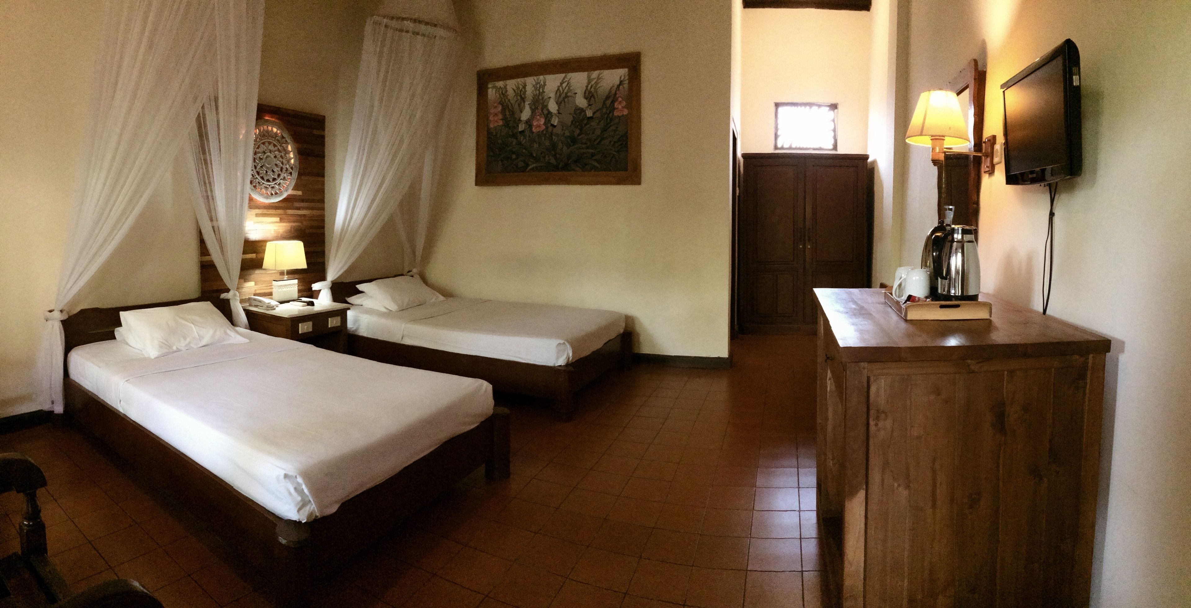 A hotel room with two single beds, a wooden cabinet, a television, and a nightstand with a lamp.