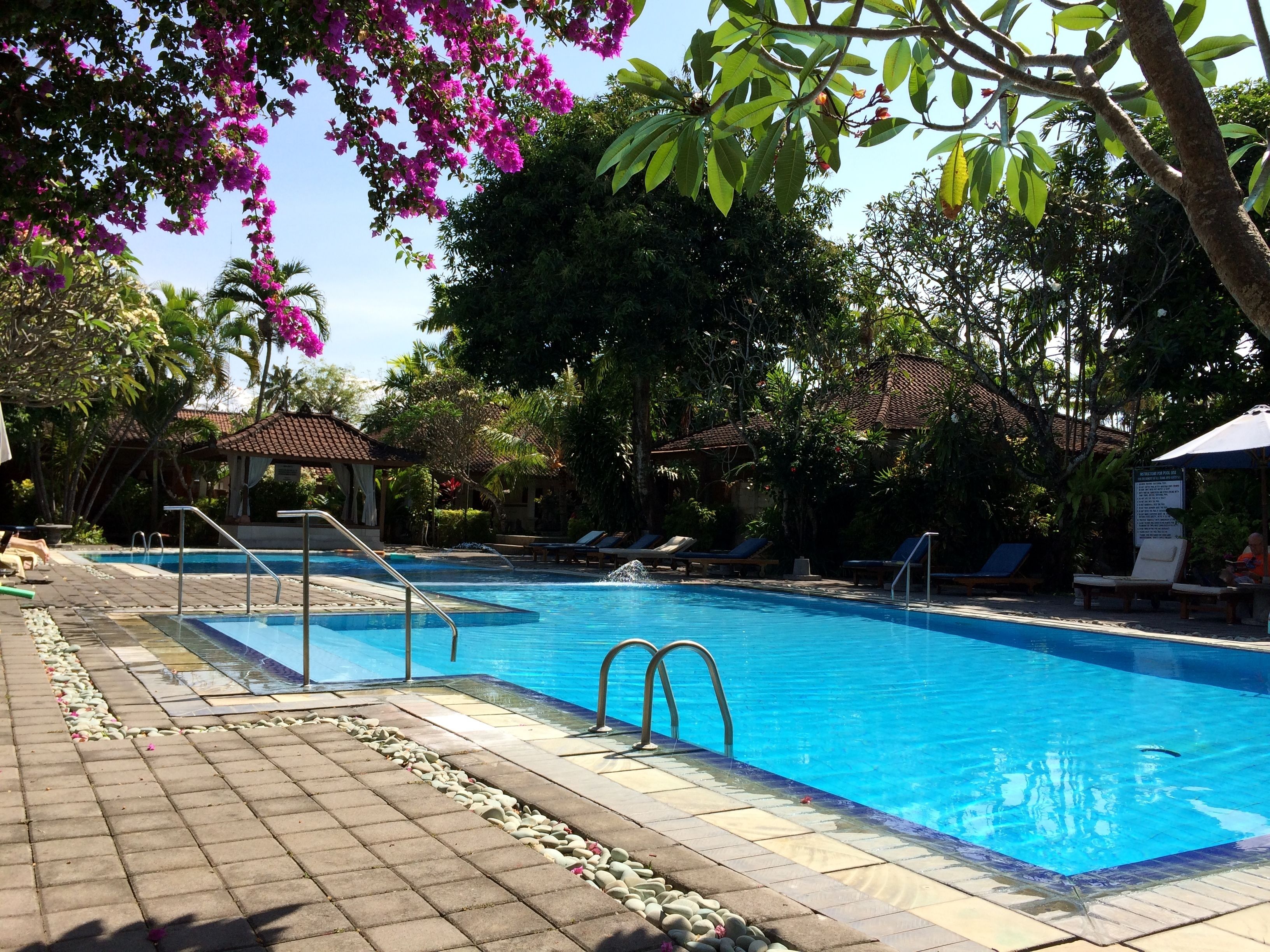Una piscina con agua cristalina azul, rodeada de sillas de descanso y un paseo enlosetado.
