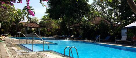 Una piscina con agua cristalina azul, rodeada de sillas de descanso y un paseo enlosetado.