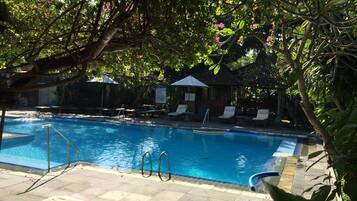 Una piscina con sillas de descanso y sombrillas, rodeada de abundante vegetación.