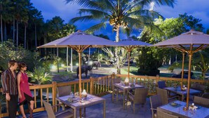 Un patio al aire libre con mesas y sillas, sombrillas y una zona de piscina.