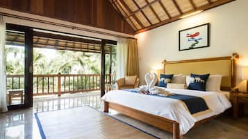 A spacious bedroom with a large bed, a wooden headboard, and a view of palm trees through the open balcony doors.