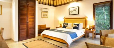 A bedroom with a bed, bedside tables, a chair, a wooden wardrobe, a framed picture on the wall, and a window with a view of trees.