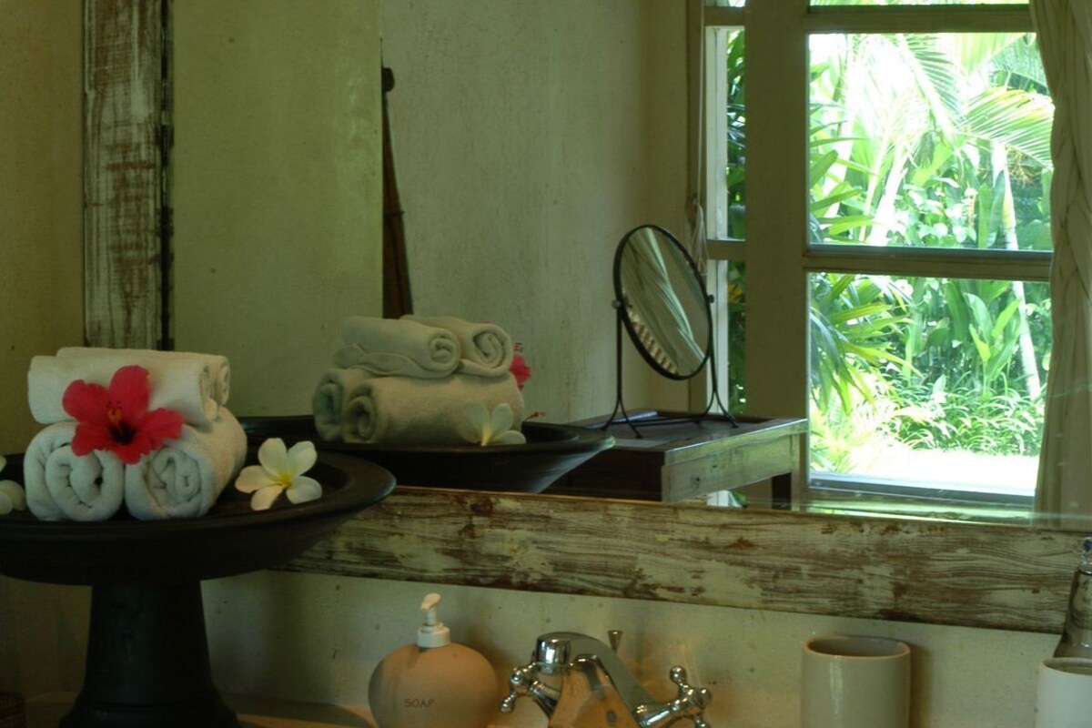 A bathroom with a sink, mirror, and window with a view of greenery.