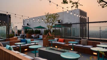 An outdoor seating area with round tables, cushioned benches, and string lights.