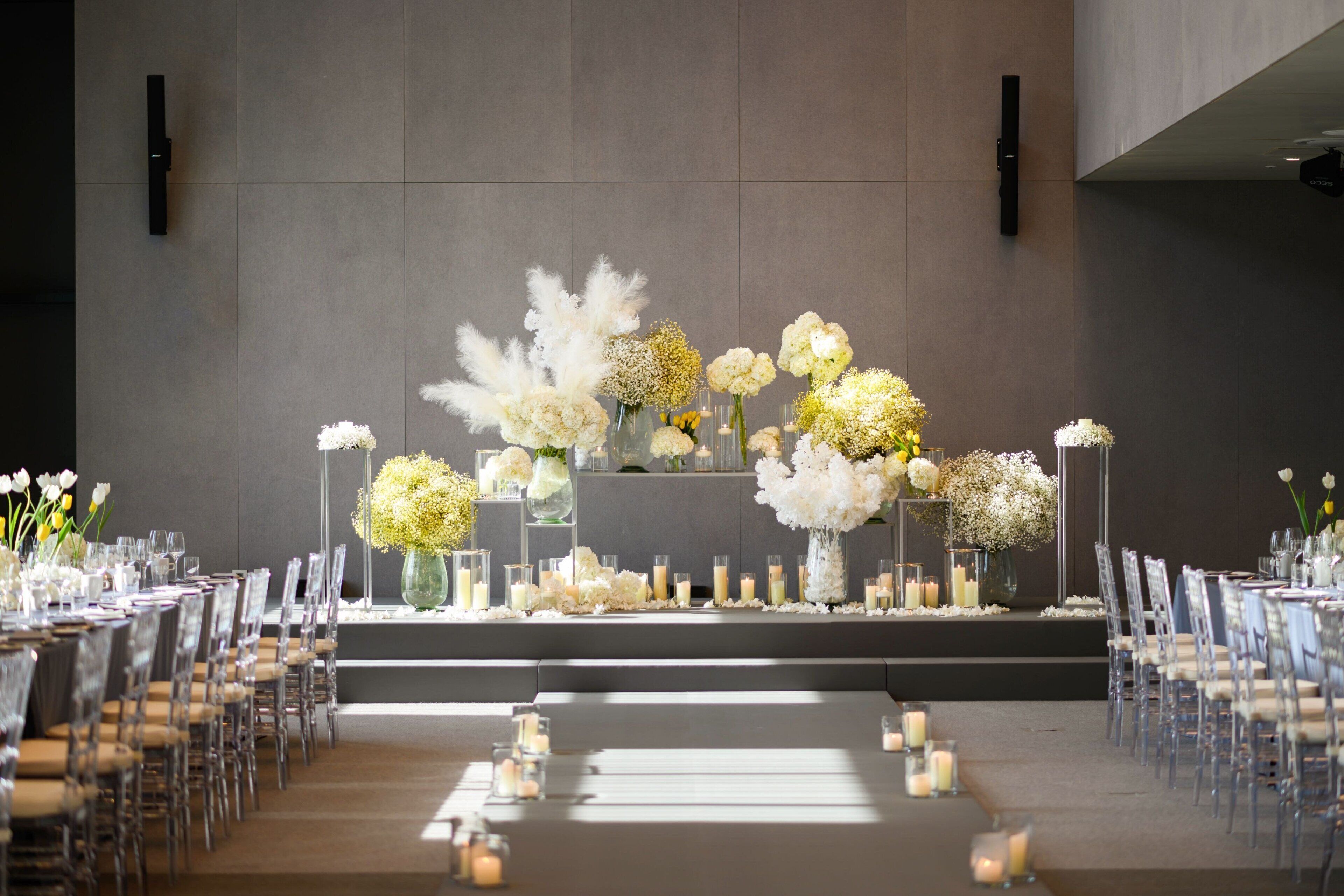 Montaje para un evento formal con una larga mesa, sillas transparentes y arreglos florales.