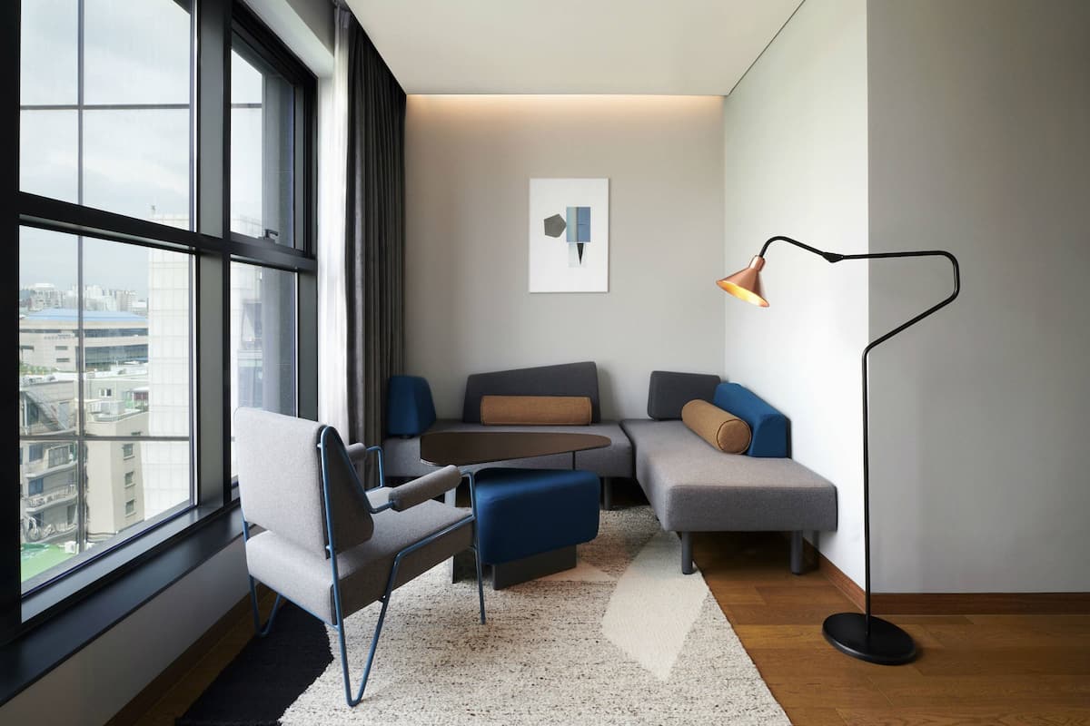 A modern living room with a large window, a sofa, a chair, a small table, and a floor lamp.